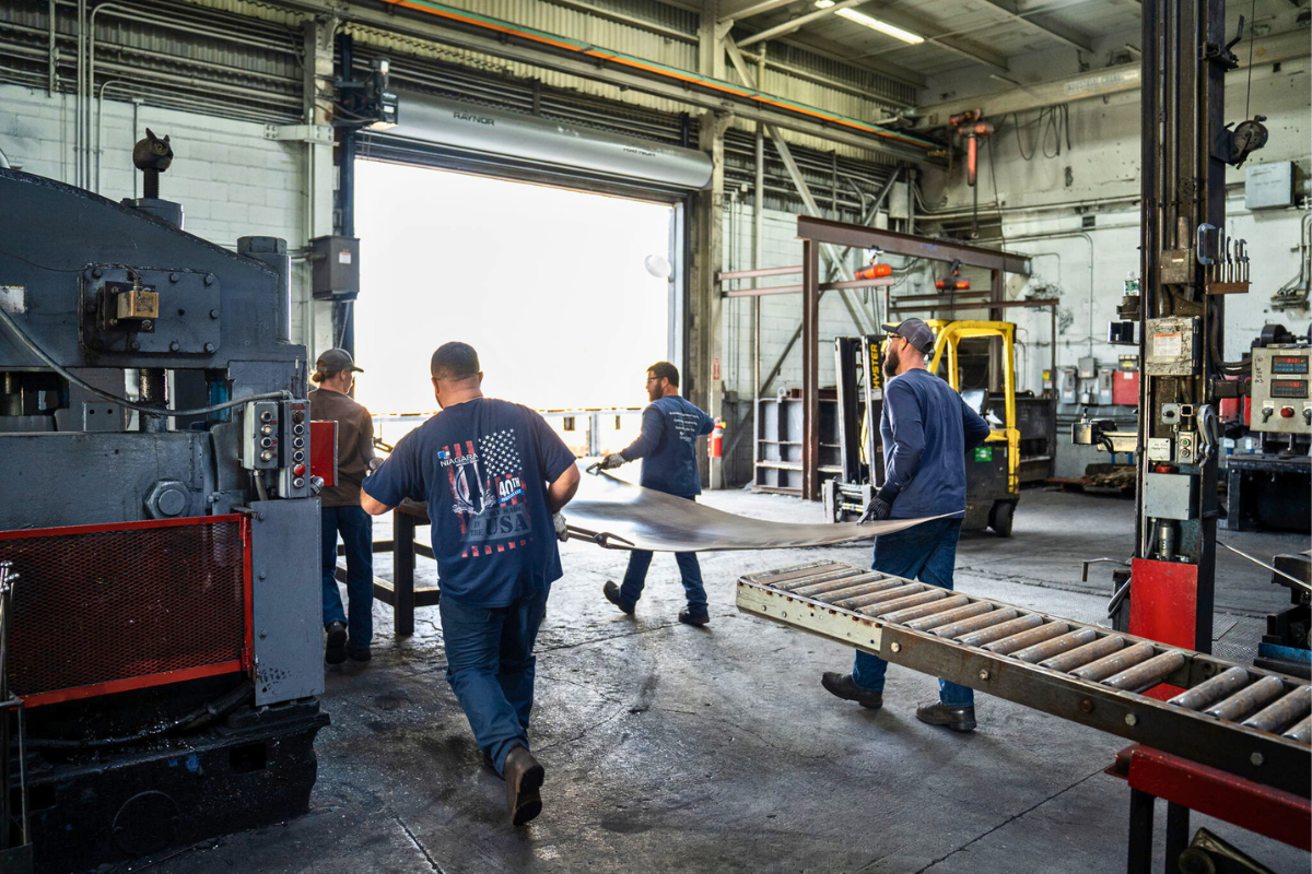 Three Niagara Specialty Metals workers carrying a titanium sheet from the press machine, supporting reliable aerospace titanium supply and team-driven precision