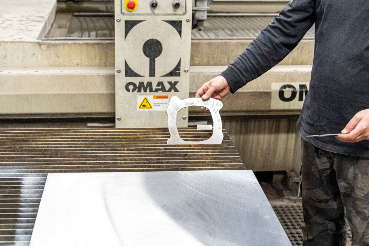 Niagara Specialty Metals employee holding water jet cut steel part, supporting the entrepreneurial journey in knife retail through precision manufacturing