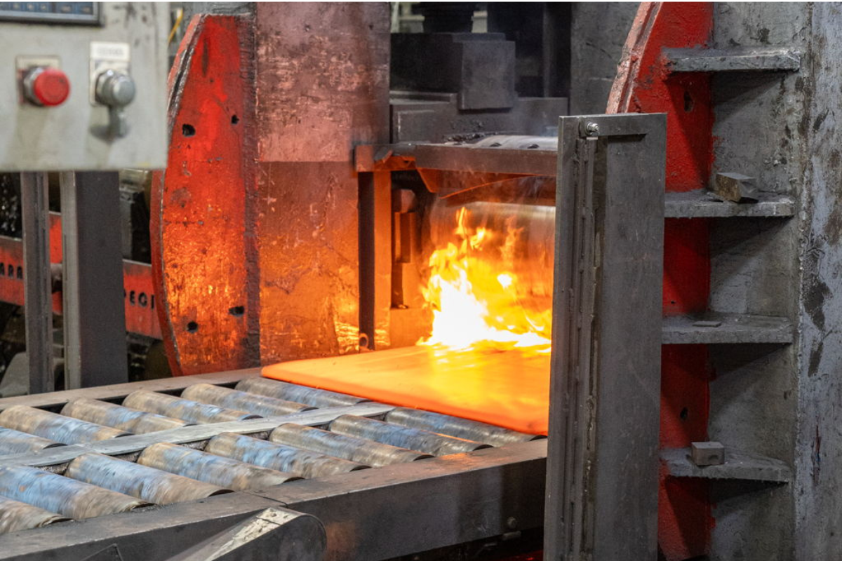 Fire blazing inside the press machine at Niagara Specialty Metals as powder metallurgy steel sheet is processed for premium knife steel production.
