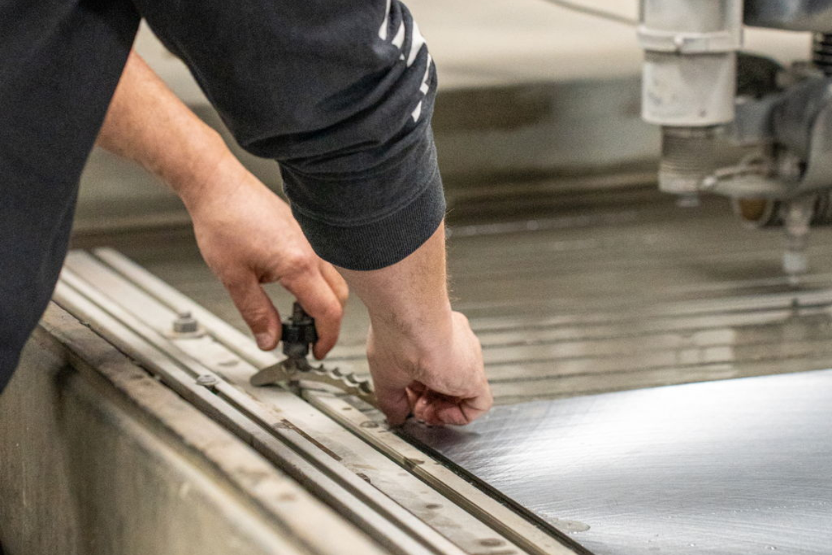 Worker operating the waterjet cutting machine at Niagara Specialty Metals, processing premium knife steel for custom knife maker applications.