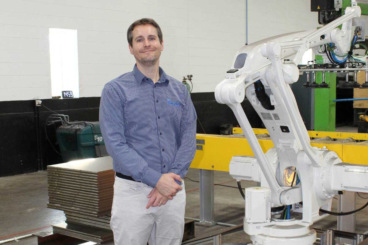Jeffrey Marshall at Niagara Specialty Metals standing in the sheet mill next to an automated robot system supporting specialty steel manufacturing and operational efficiency.