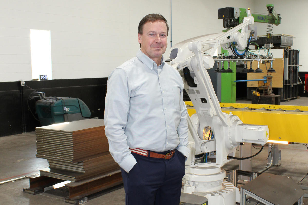 Bob Shabala at Niagara Specialty Metals standing in the sheet mill next to an automated robot system supporting advanced specialty steel processing and manufacturing innovation.