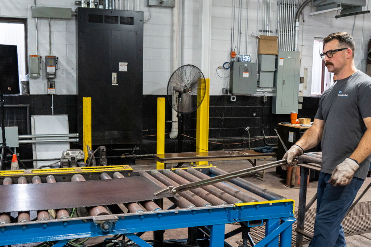 Niagara Specialty Metals worker handling processed specialty steel sheet, illustrating steel toughness vs strength in knife and aerospace applications