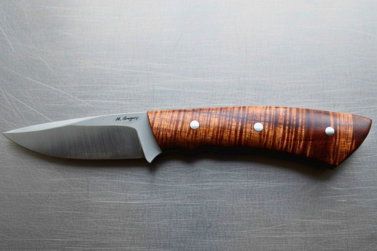 Finished fixed-blade knife with a wood handle displayed on a metal surface during Carl Stroud’s Cutlery Symposium presentation.